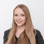 Eine Person mit langen, glatten blonden Haaren lächelt in die Kamera. Sie trägt eine schwarze Lederjacke und ein schwarzes Oberteil. Der Hintergrund ist schlicht weiß.