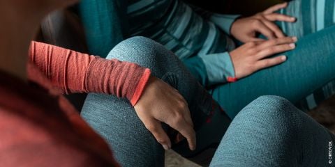 Zwei Personen sitzen eng beieinander und tragen langärmlige Oberteile mit Strukturmuster und Leggings in Rot- und Blautönen. Ihre Hände ruhen auf ihren Knien, wodurch der detaillierte Stoff und die bequeme Passform der Kleidung zur Geltung kommen.