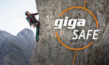 Ein Kletterer mit Helm und Ausrüstung erklimmt eine steile Felswand. Im Vordergrund steht in fetten weißen und orangefarbenen Buchstaben der Text „giga SAFE“. Im Hintergrund sind Berggipfel zu sehen.