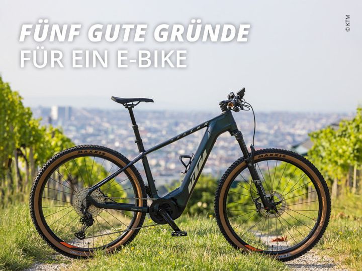 Ein schwarzes E-Bike steht auf einem Grasweg in einem Weinberg. Im Hintergrund ist eine Stadtlandschaft unter einem strahlend blauen Himmel zu sehen. Der Text auf dem Bild lautet „Fünf gute Gründe für ein E-Bike“.