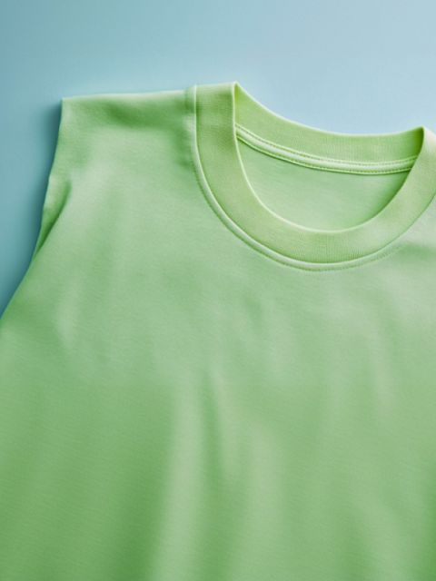 Nahaufnahme eines ordentlich gefalteten hellgrünen T-Shirts auf hellblauem Untergrund. Das T-Shirt hat kurze Ärmel mit Rundhalsausschnitt und der Stoff wirkt glatt und weich.