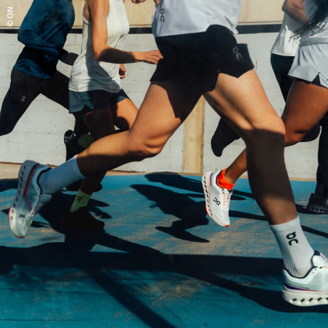 Eine Gruppe von Menschen läuft im Freien in Sportkleidung und Turnschuhen. Das Bild konzentriert sich auf die Bewegung ihrer Beine und Füße, wobei das Sonnenlicht Schatten auf den Boden wirft.