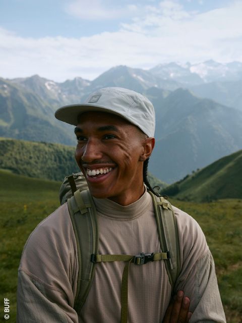 Ein Mann in Outdoor-Ausrüstung klettert einen felsigen Untergrund hinauf. Er trägt eine hellgrüne Jacke, schwarze Hosen und einen schwarzen Rucksack. Oben steht „NACHHALTIGES FÜR HERREN“ und an der Seite ein kleines „ADIDAS“.