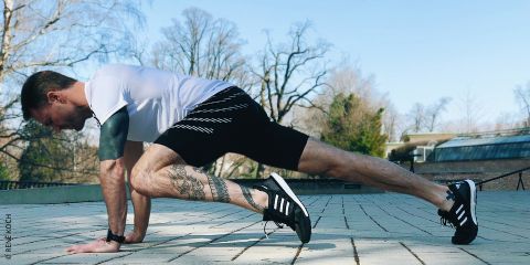 Ein Mann in Sportkleidung macht an einem sonnigen Tag im Freien eine Ausfallschrittübung. Der Text lautet „Kraftübungen für Laufsport-Fans“. Im Hintergrund sind Bäume und ein Gebäude zu sehen.