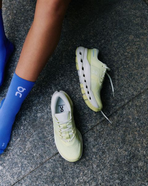 Eine Person mit einer blauen Socke steht neben einem Paar hellgelber Laufschuhe auf einem grauen Steinboden.