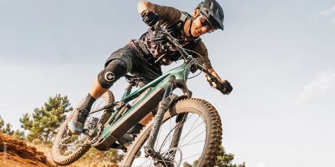 Ein Radfahrer mit Schutzausrüstung fährt an einem sonnigen Tag mit seinem Mountainbike einen unbefestigten Weg hinunter und neigt sich scharf in eine Kurve.
