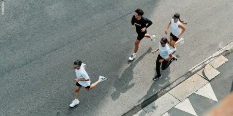 Vier Personen laufen gemeinsam auf einer gepflasterten Straße, von oben gesehen, in Sportkleidung und Turnschuhen.